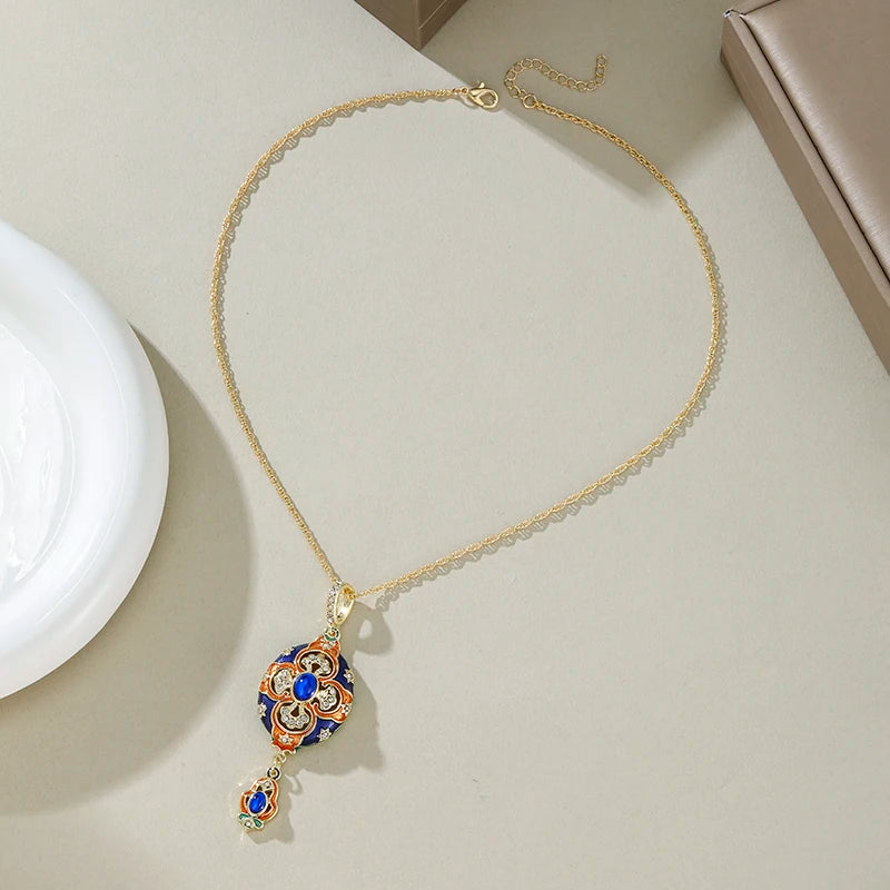 Gold necklace with a blue pendant on a light beige surface