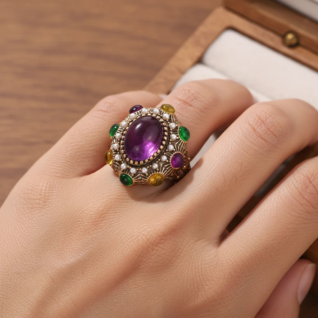 Gold open ring with oval purple gemstone, pearl-like stones, and green accents