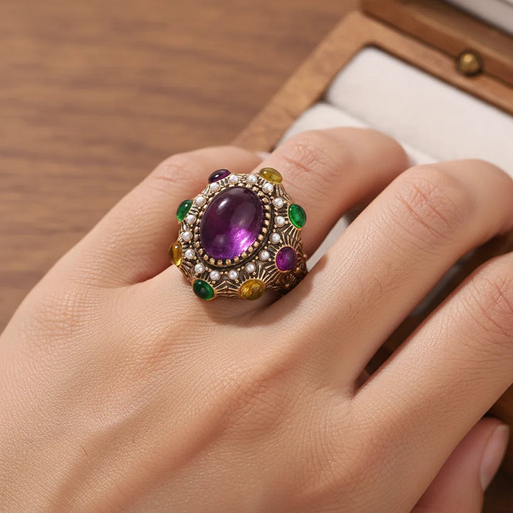 Gold open ring with oval purple gemstone, pearl-like stones, and green accents