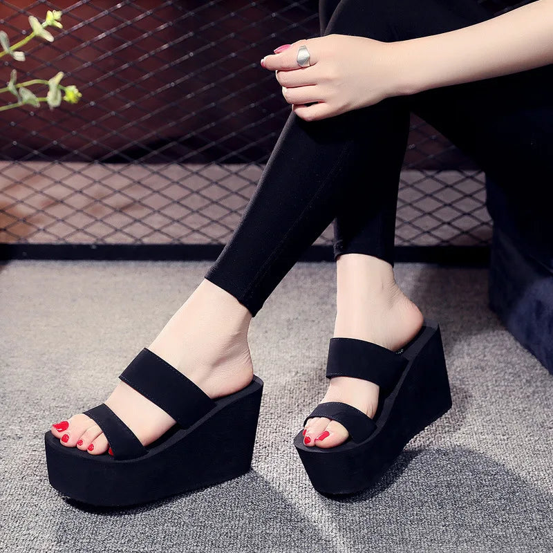 Person wearing black platform sandals on a textured floor.