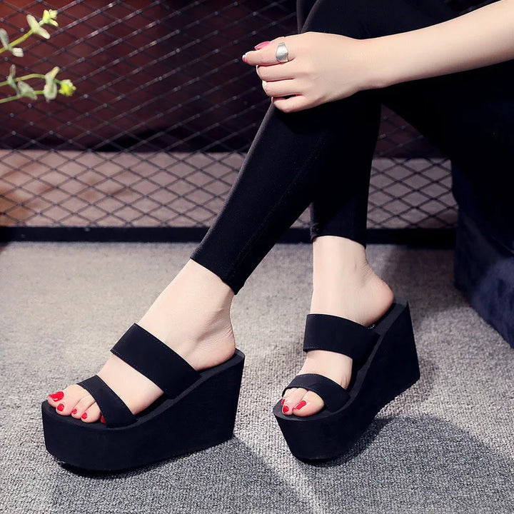 Person wearing black platform sandals on a textured floor.
