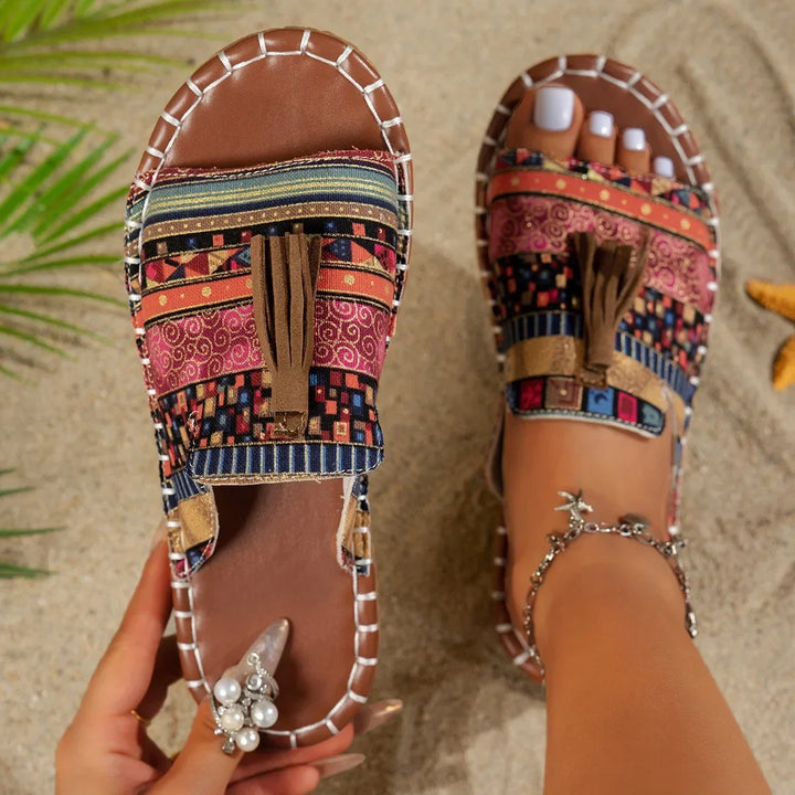 Colorful sandals with a patterned sole worn on a sandy background