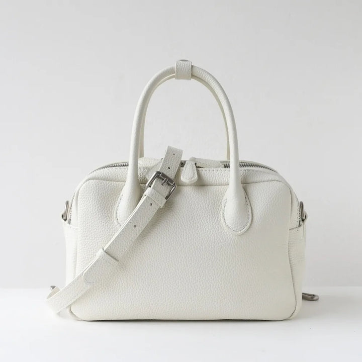 A structured white pebbled leather handbag with dual top handles and a matching shoulder strap, photographed against a clean white studio background.