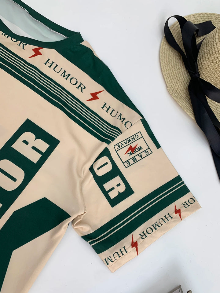 T-shirt sleeve close-up with dark green 'HUMOR' text stripes and small patch label