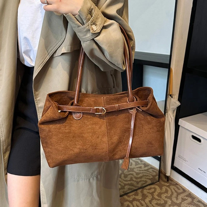 Women’s suede tote bag in brown, held by a hand with crossbody-style strap.