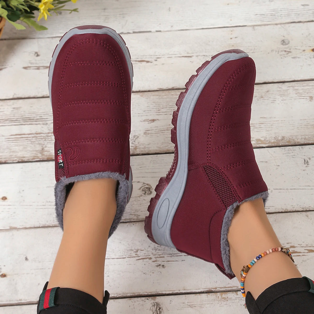 Maroon winter boots with gray fur lining worn on a wooden floor.