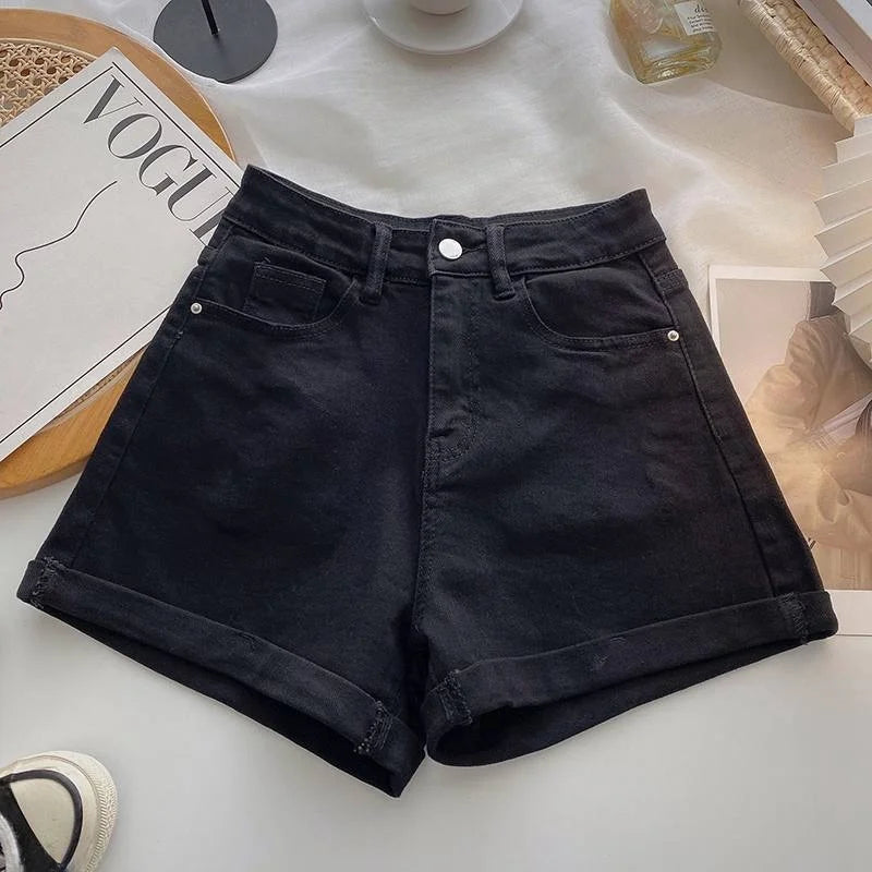 Black denim shorts on a white surface with a magazine and other items in the background