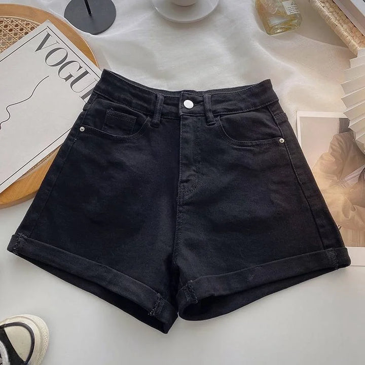 Black denim shorts on a white surface with a magazine and other items in the background