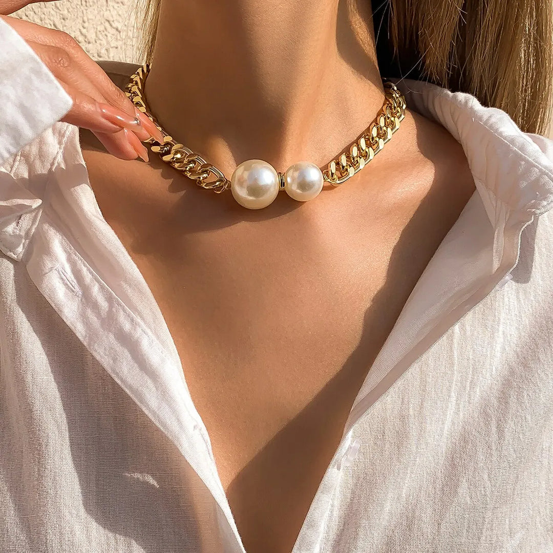 Gold chain necklace with pearls worn by a person in a white shirt.