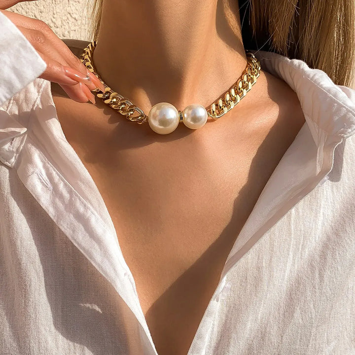 Gold chain necklace with pearls worn by a person in a white shirt.