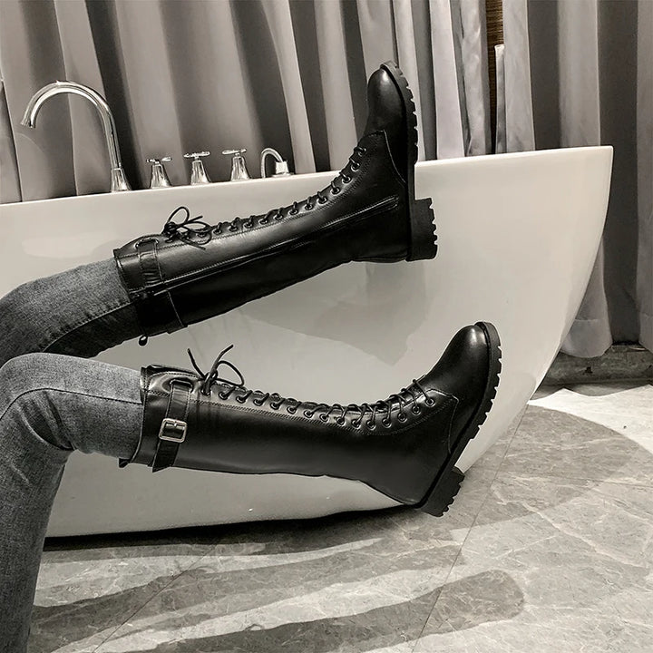 Person wearing black knee-high boots with laces, sitting on a white bathtub.