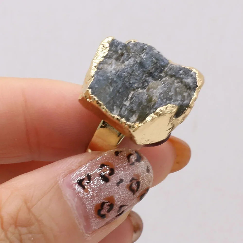 Gold ring with a rough stone held by a hand with patterned nails on a light background