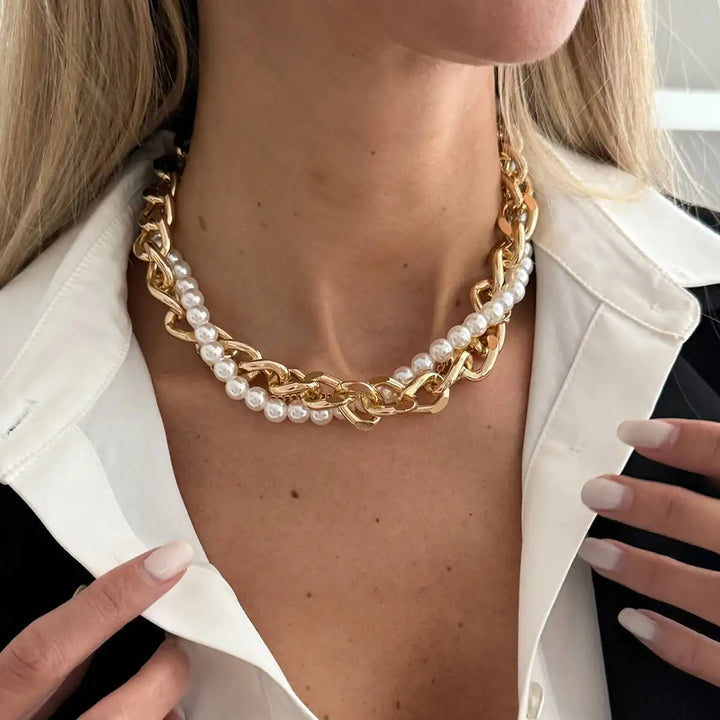 Gold chain and pearl necklace worn by a person with a white jacket.
