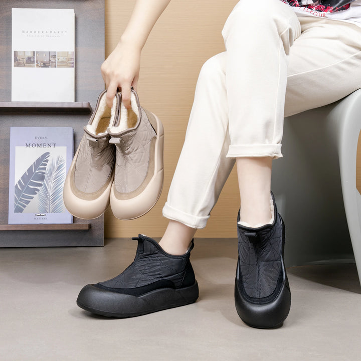 Person holding a pair of beige shoes next to black shoes on a neutral background