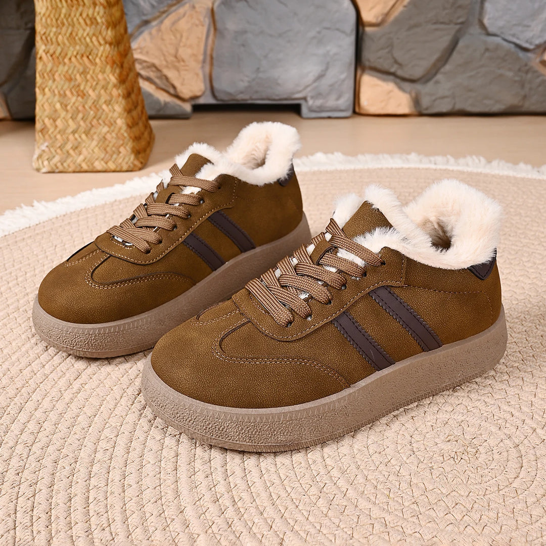 A pair of women's low-top casual sneakers in brown suede with dark brown side stripes, featuring a thick beige sole and fluffy white faux-fur lining around the collar, displayed on a woven rug.