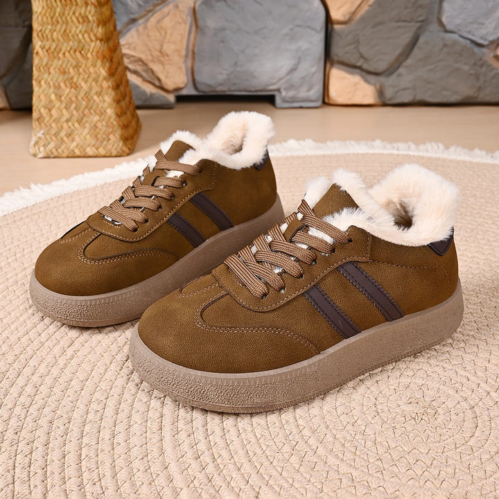 A pair of women's low-top casual sneakers in brown suede with dark brown side stripes, featuring a thick beige sole and fluffy white faux-fur lining around the collar, displayed on a woven rug.