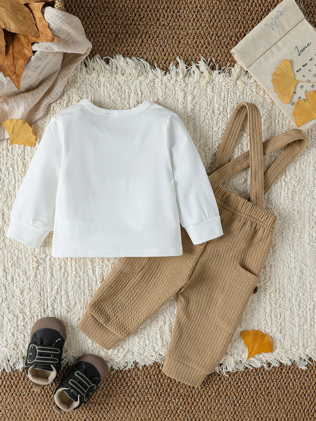 Children's white shirt and brown suspenders with shoes on a textured surface