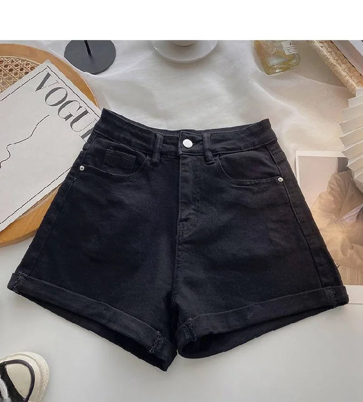 Black denim shorts on a white surface with a magazine and other items in the background