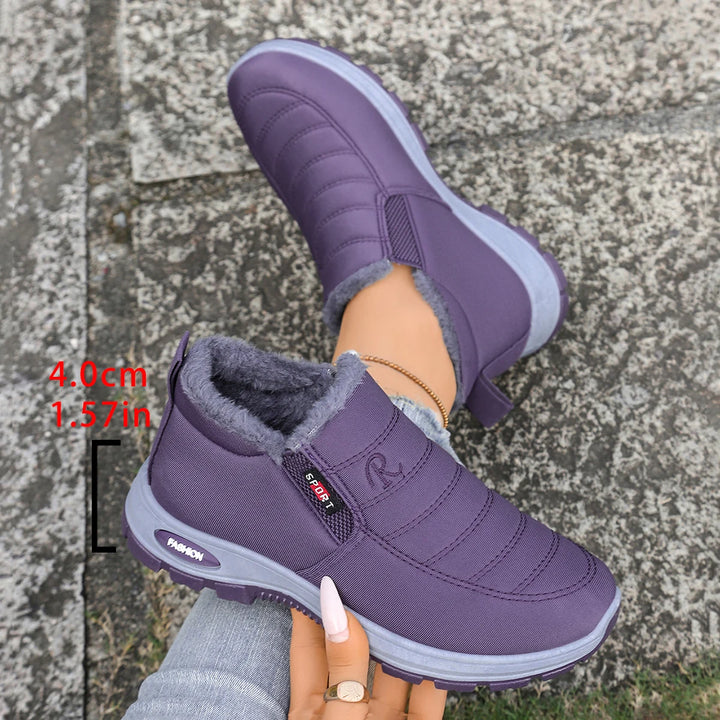 Purple winter shoes with gray lining held by a person on a stone pavement.