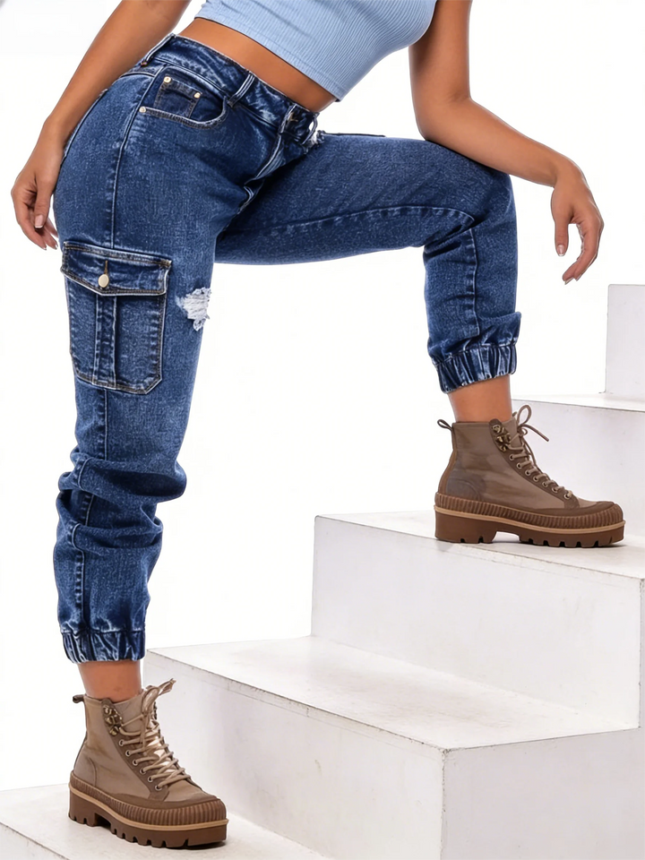 Dark blue denim jeans with side cargo pockets, ripped knee panels, and cuffed ankle hem.