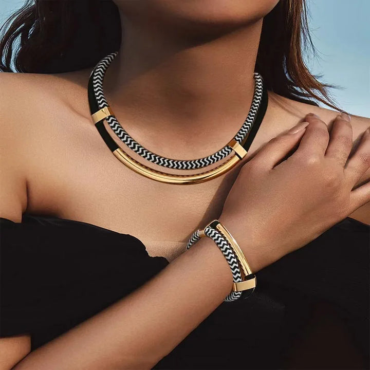 Person wearing a gold and black patterned necklace and bracelet against a blurred background
