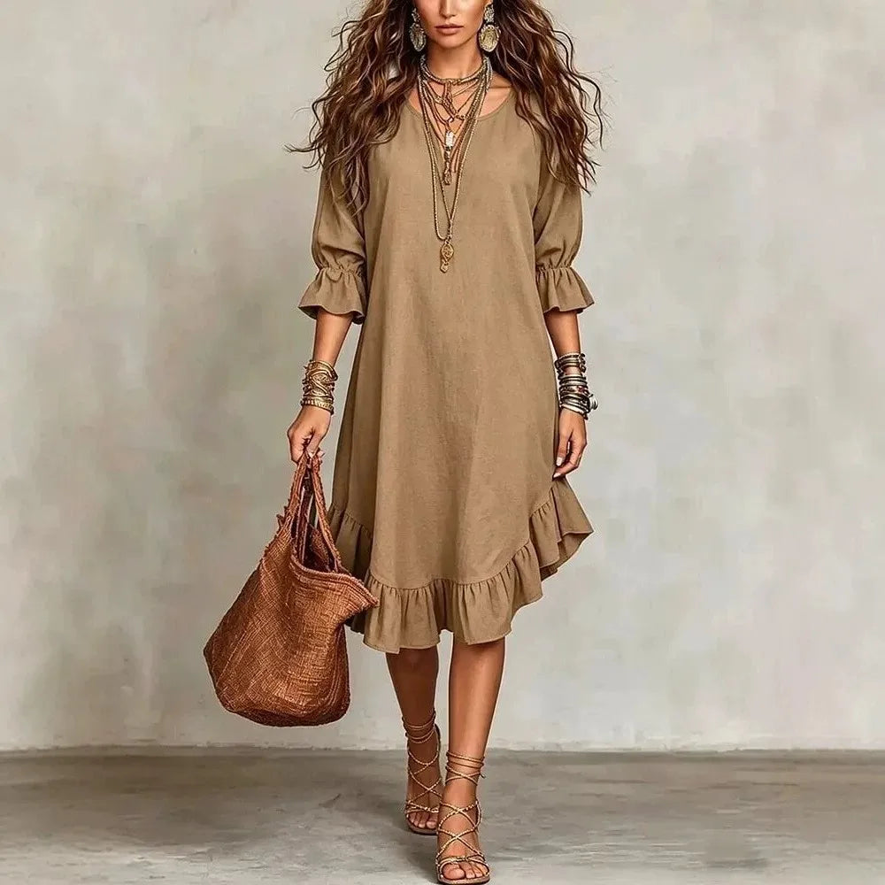 Woman wearing a beige dress holding a brown bag against a plain background
