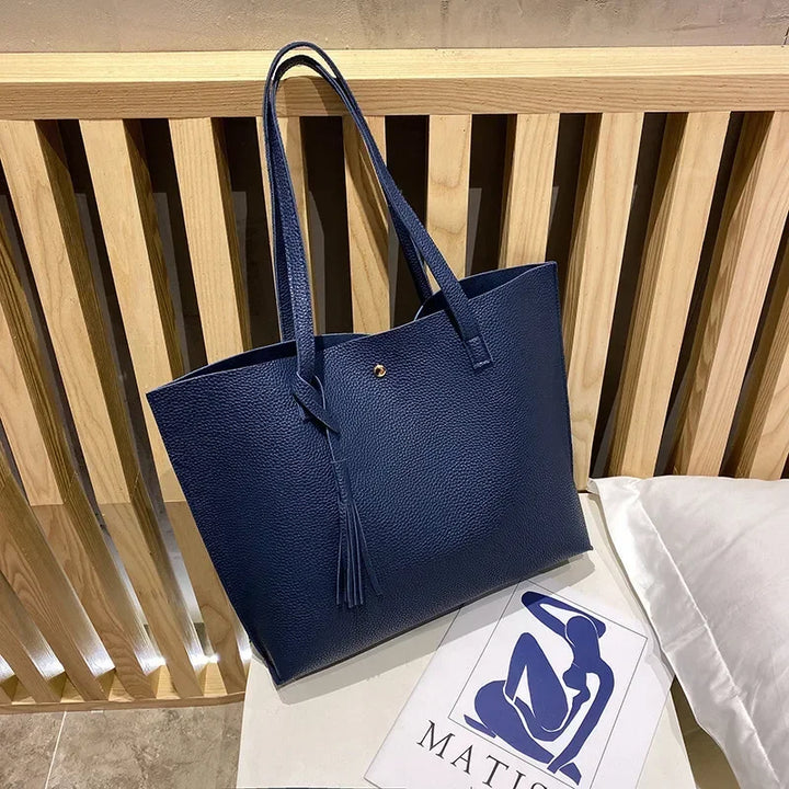Blue tote bag on a wooden surface with a white pillow and magazine underneath.