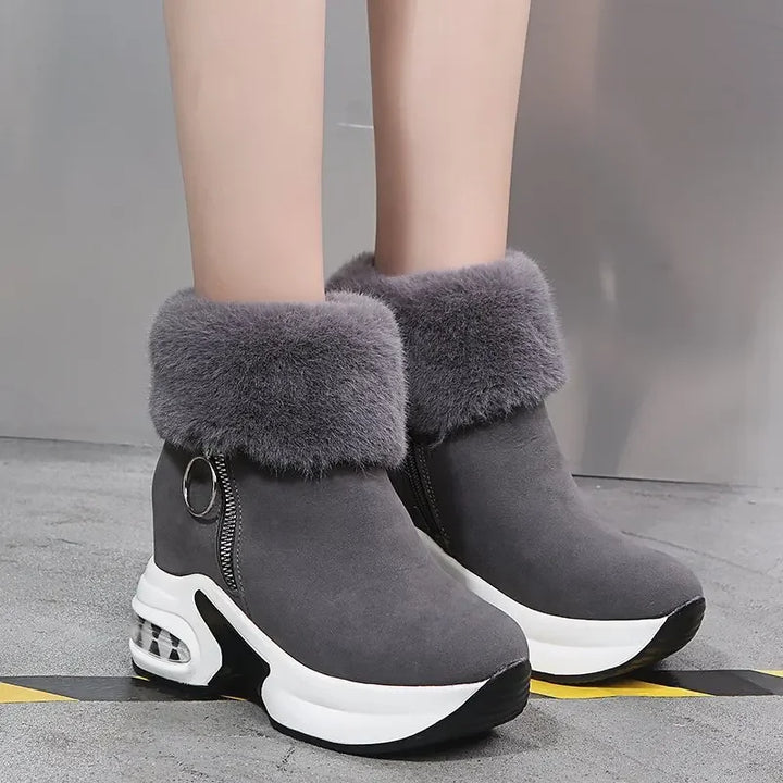 Gray winter boots with fur trim worn by a person on a gray floor.