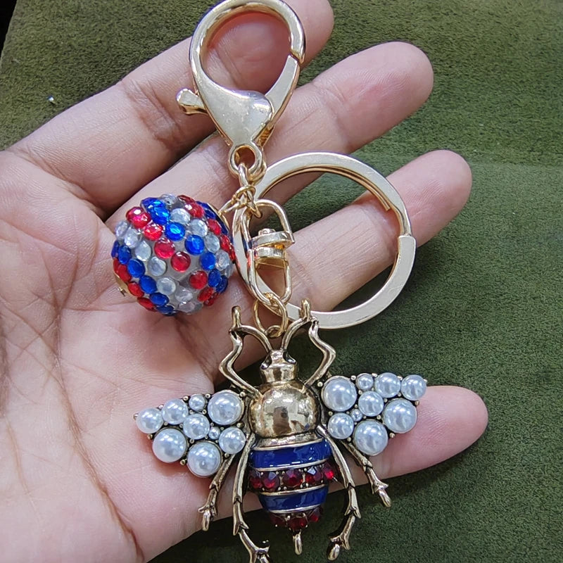 Keychain with bee and ball design held in a hand against a green background