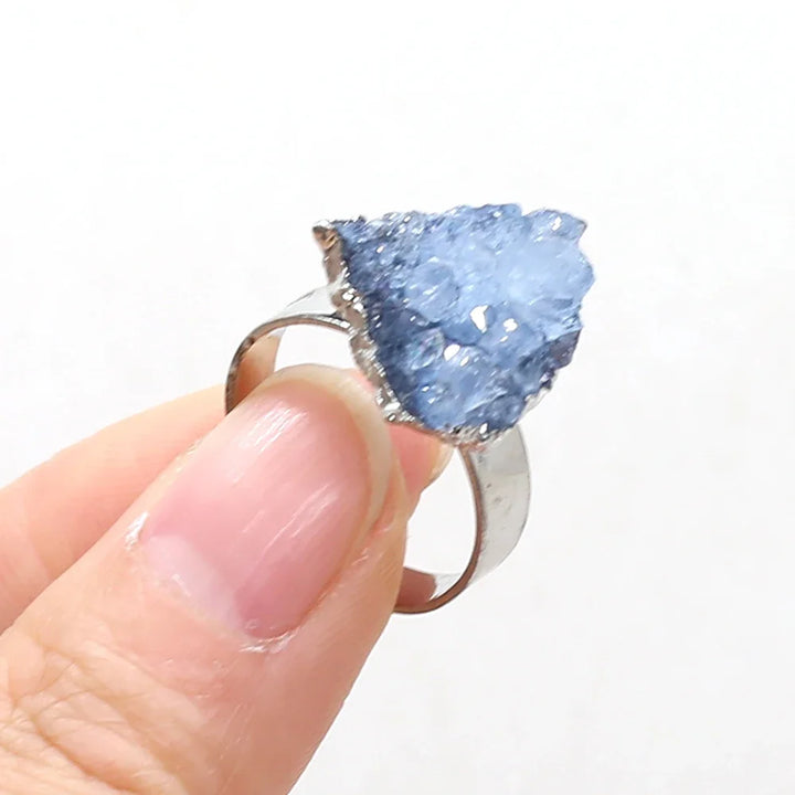 Ring with a blue crystal held by a hand on a white background