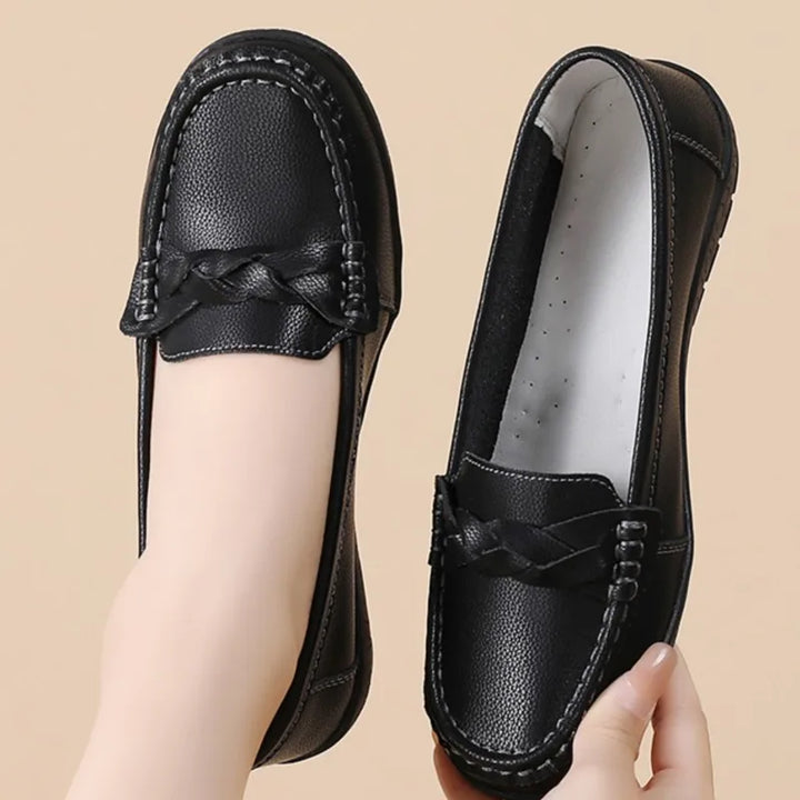 Black leather loafers with a braided detail on a beige background
