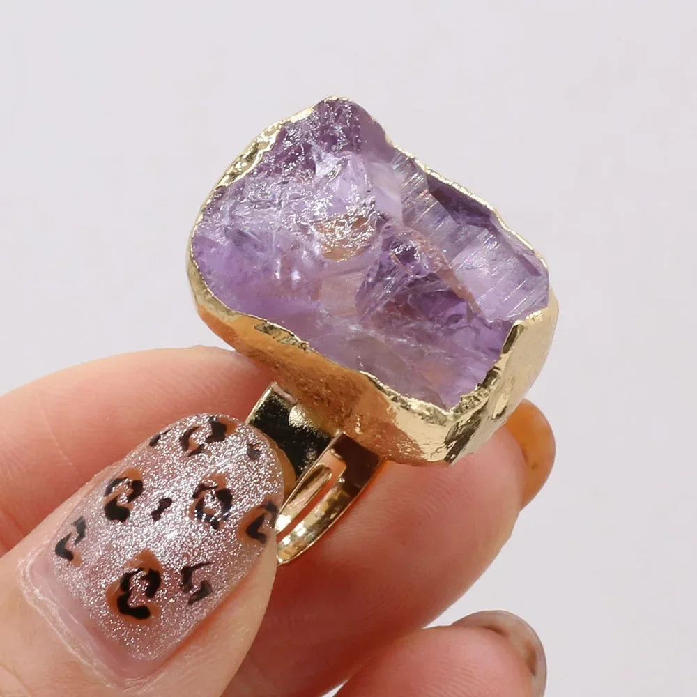 Gold ring with a purple crystal held by a hand against a white background