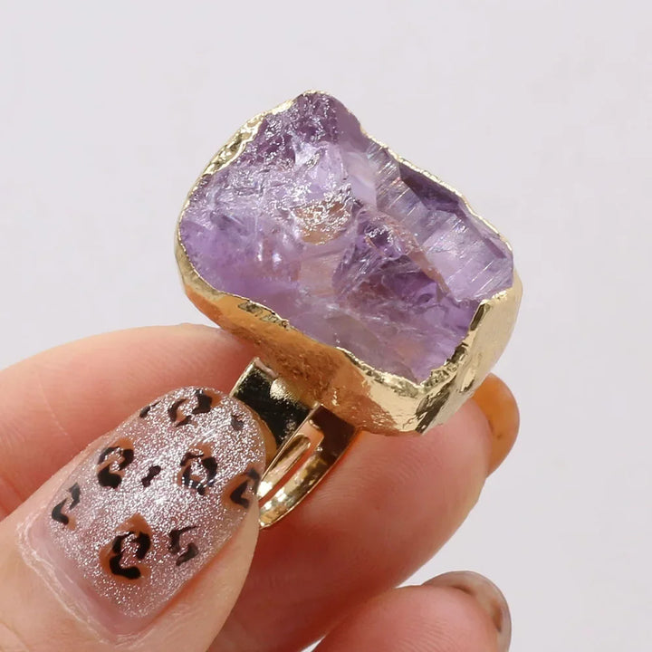 Gold ring with a purple crystal held by a hand against a white background