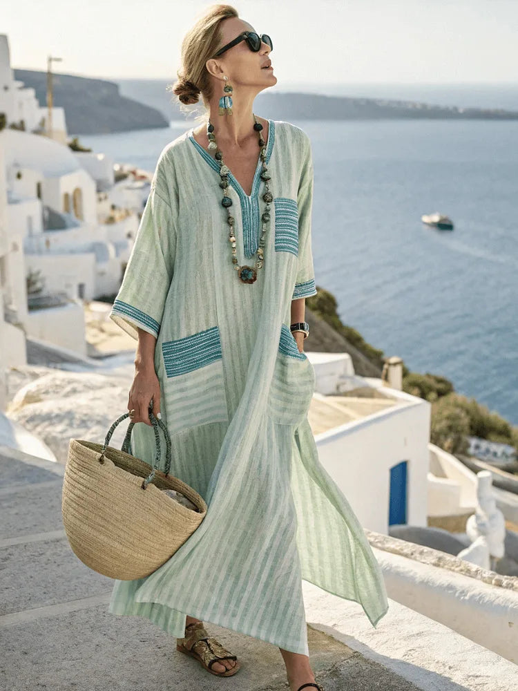 Woman in a light green dress with blue accents standing in a scenic location with ocean and buildings.