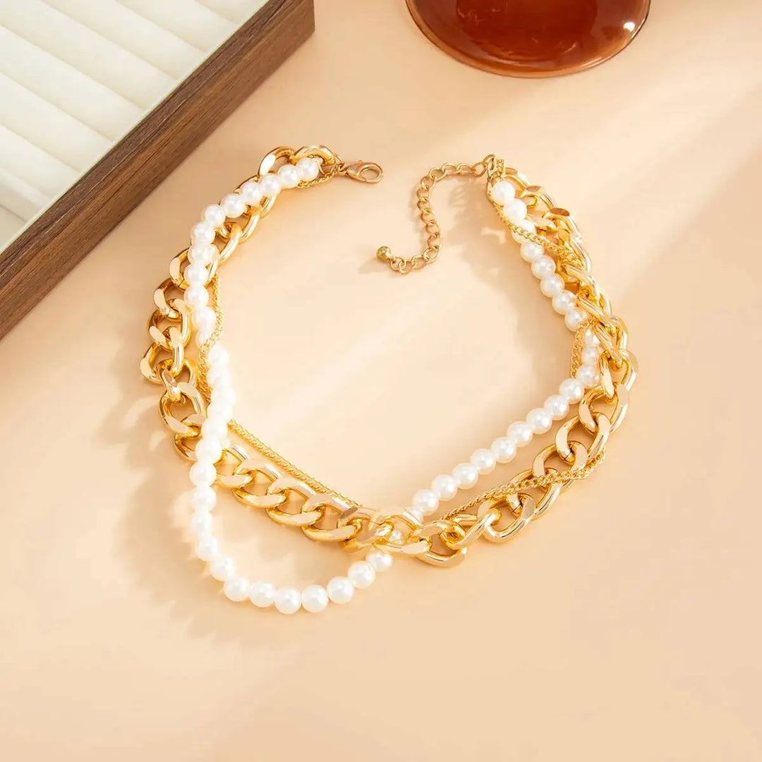 Gold chain and pearl necklace on a beige surface