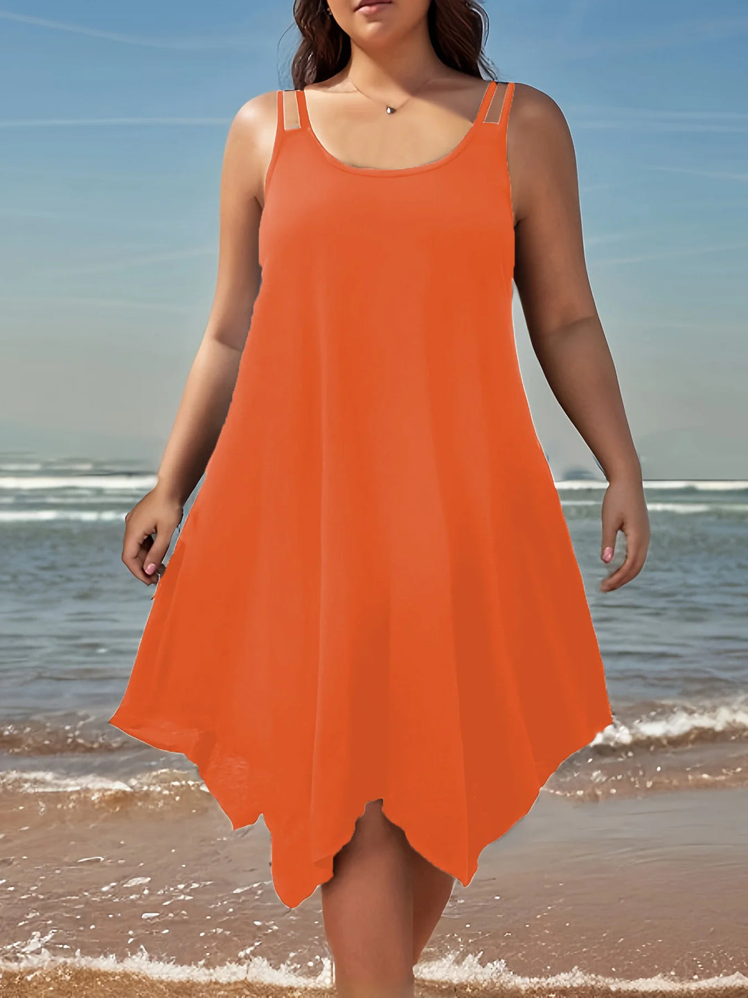 Woman wearing an orange dress standing on a beach with ocean waves in the background