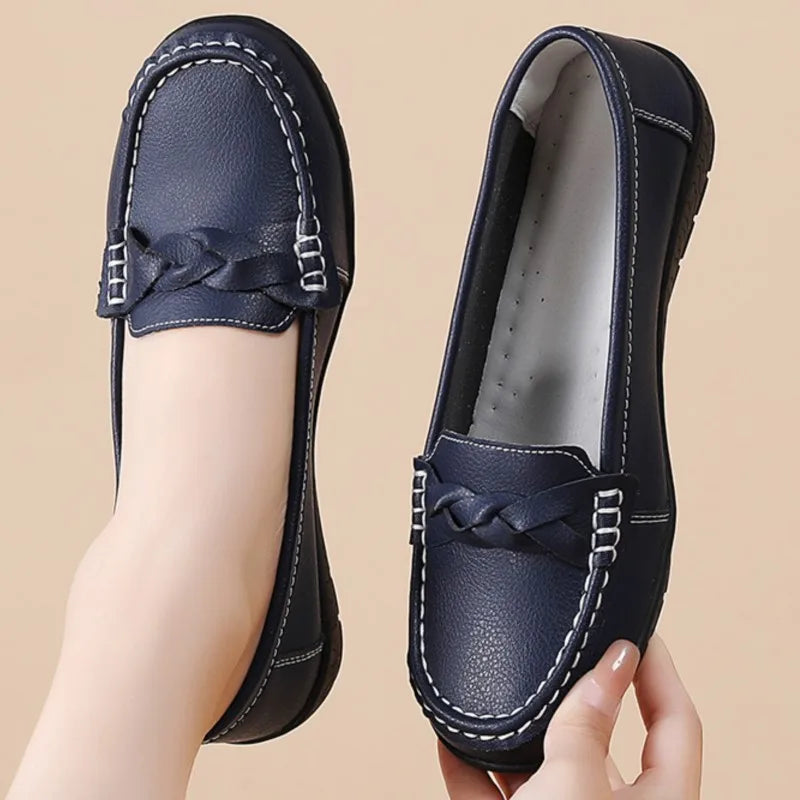 Navy blue loafers with braided detail held by a hand on a beige background