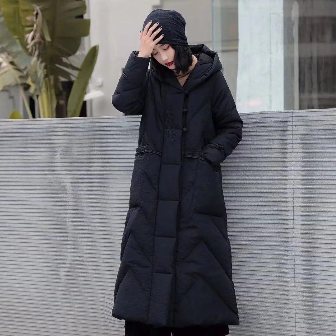 Person wearing a long black puffer coat standing against a light-colored wall.
