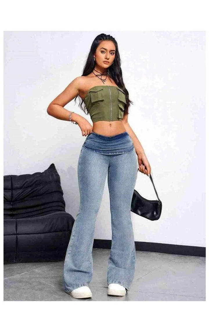 Woman wearing a green top and blue jeans holding a black handbag against a white background