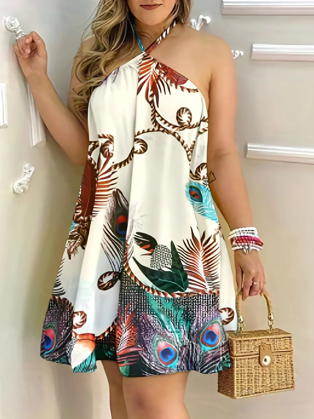Woman wearing a colorful halter neck dress with peacock feather pattern, holding a small woven bag.