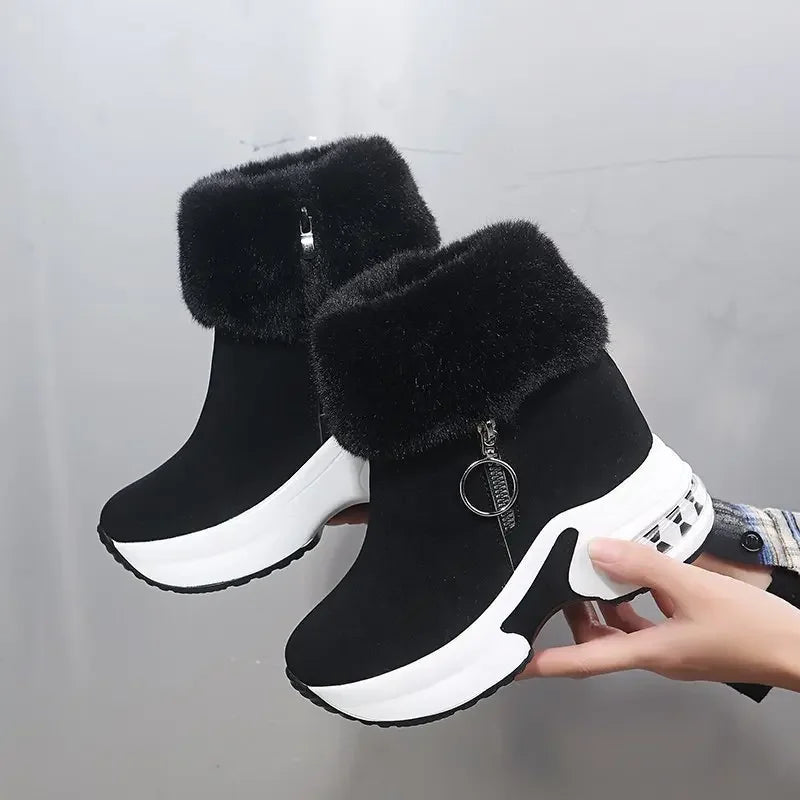 Black ankle boots with white soles held by a hand against a gray background