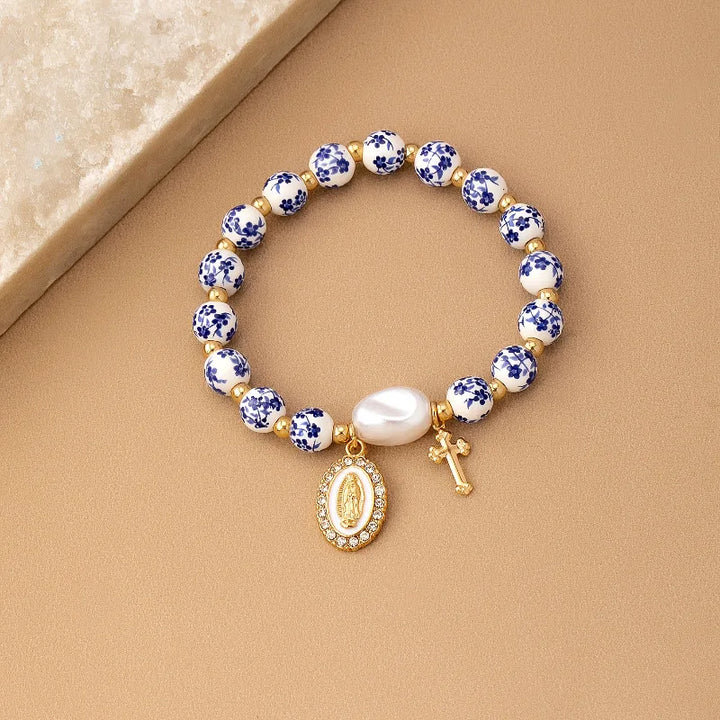 Bracelet with blue floral beads, gold accents, and religious charms on a wooden surface.