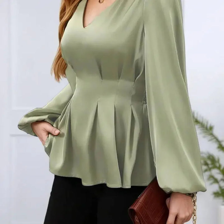 Woman wearing a green peplum top with long sleeves against a neutral background