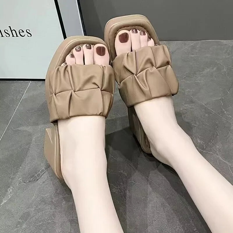 Beige quilted sandals worn on a gray floor.