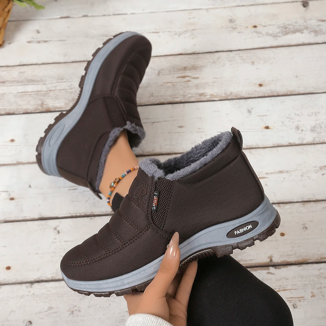 Brown winter boots with gray lining held by a hand on a wooden floor.
