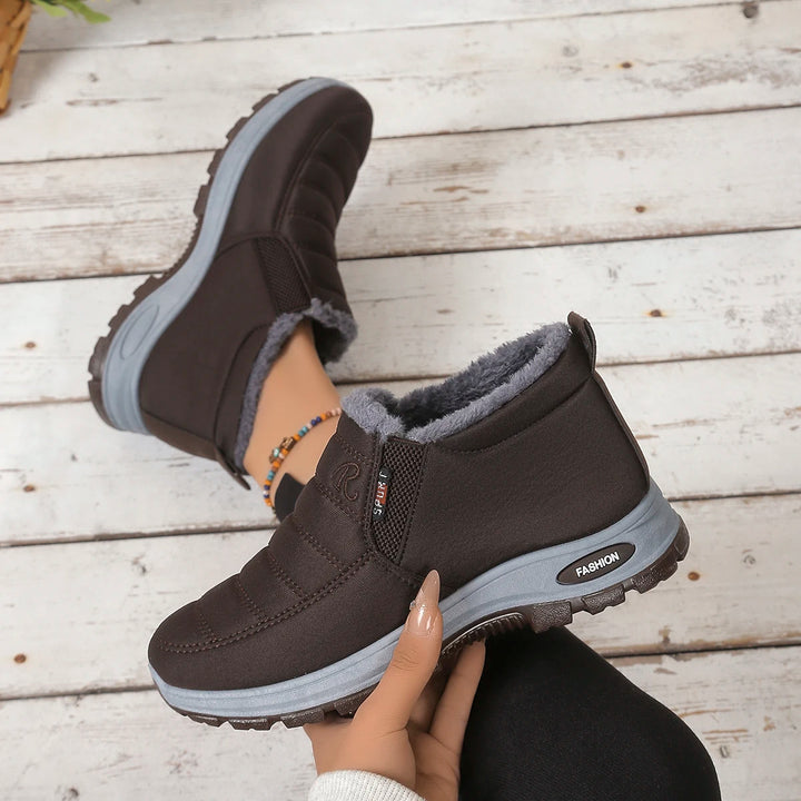 Brown winter boots with gray lining held by a hand on a wooden floor.