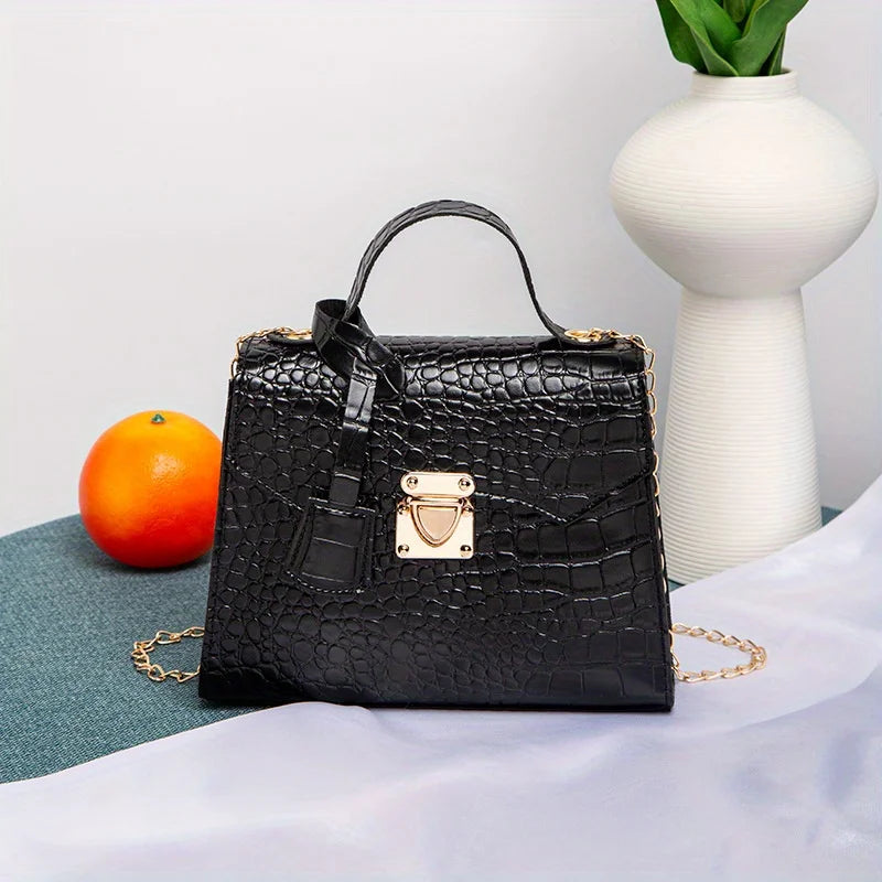 Black crocodile-patterned handbag with gold accents on a light gray surface with an orange and white vase in the background.
