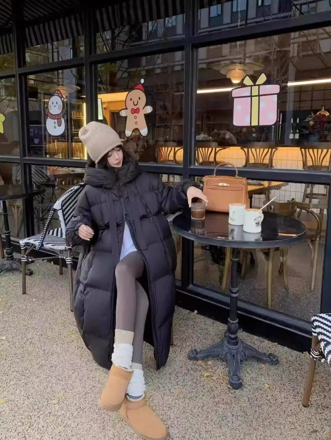 Person wearing a long black coat sitting outside a cafe.