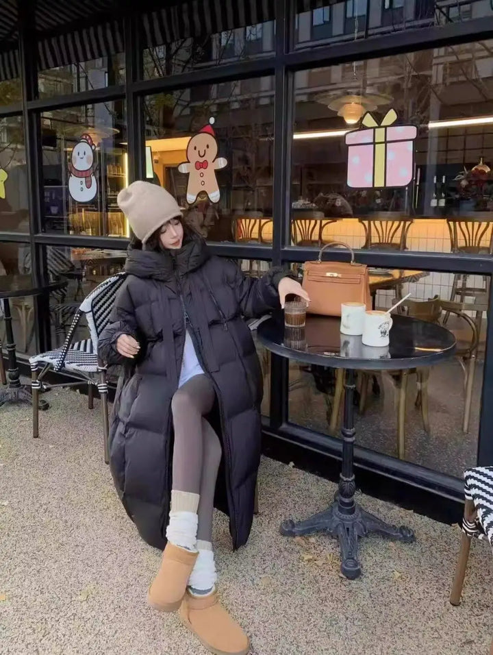 Person wearing a long black coat sitting outside a cafe.
