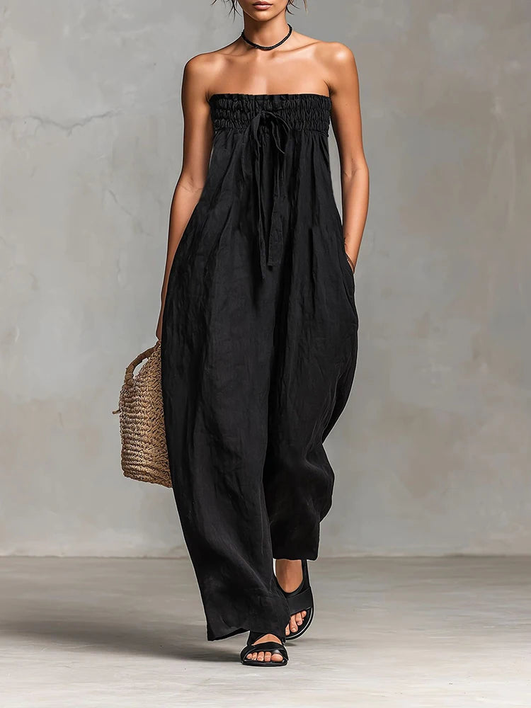 Woman wearing a black strapless jumpsuit with a woven bag against a neutral background